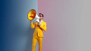 Ein Mann in gelbem Anzug und mit Sonnenbrille ruft etwas durch ein Megaphon.